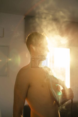 Foto de Retrato de un joven guapo planchando su pecho con ropa de hierro - Imagen libre de derechos