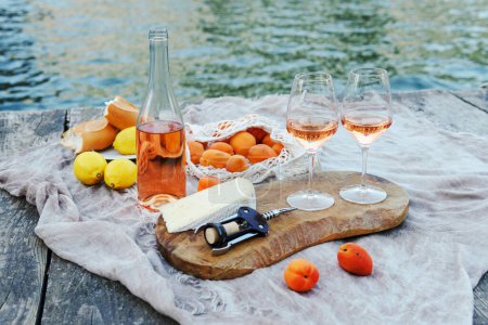 Photo for Rose wine, fruits and snacks on the wooden pier during picturesque picnic on the wooden gondola dock - Royalty Free Image