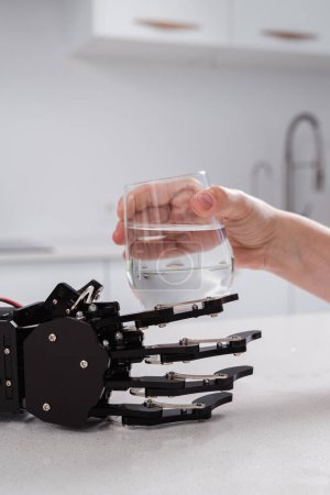 Téléchargez les photos : Aide-soignant robotique étendant une main avec un verre d'eau à une jeune femme. - en image libre de droit