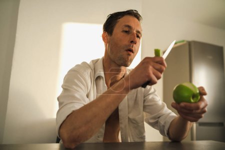 Foto de Retrato cinematográfico del hombre guapo cortando y comiendo manzana - Imagen libre de derechos