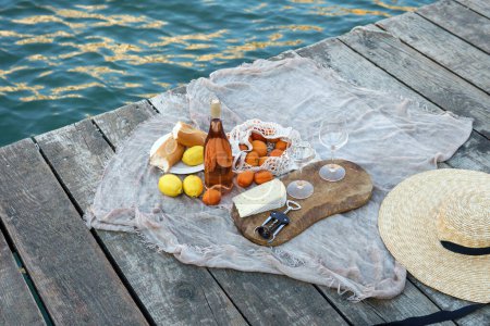 Photo for Rose wine, fruits and snacks on the wooden pier during picturesque picnic on the wooden gondola dock - Royalty Free Image