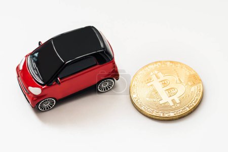 Foto de Coche de juguete rojo junto a un bitcoin dorado sobre fondo blanco - Imagen libre de derechos