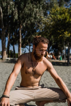 Téléchargez les photos : Jeune homme barbu échauffement avant son entraînement sur la plage - en image libre de droit