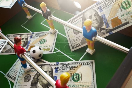 Téléchargez les photos : Jeu de baby-foot avec des billets en dollars éparpillés autour, faisant allusion à un concept de pari et à la victoire - en image libre de droit