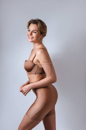 Foto de Retrato de mujer atractiva joven con lencería marrón con calzoncillos de cintura alta sobre fondo gris. - Imagen libre de derechos