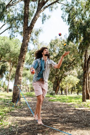 Foto de Joven confiado haciendo malabarismos y equilibrándose en el slackline en el parque de la ciudad durante el día de verano - Imagen libre de derechos