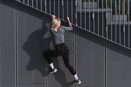 Photo for Young woman athlete climbing on metal wall during her street workout. - Royalty Free Image