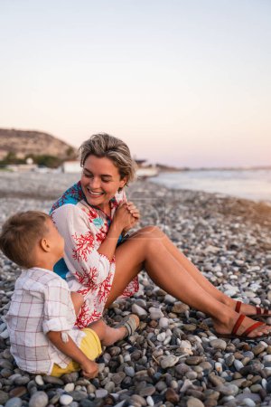Photo for Mother and her cute little son collecting pebbles on shingle beach. - Royalty Free Image