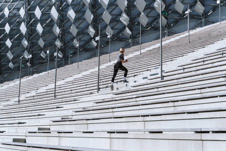 Téléchargez les photos : Athlète femme portant des vêtements de sport féminins courant et faisant de l'exercice sur un escalier entre les gradins du stade extérieur. - en image libre de droit