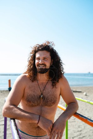 Téléchargez les photos : Portrait de joyeux homme torse nu bouclé faisant de l'exercice sur la plage - en image libre de droit