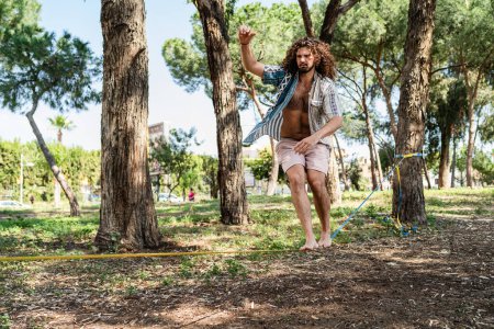 Téléchargez les photos : Jeune homme confiant relâchement dans le parc de la ville pendant la journée d'été - en image libre de droit