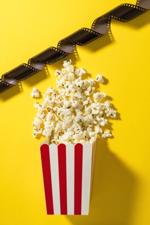 Photo for Classic striped bucket with delicious popcorn and film stock on yellow background. - Royalty Free Image