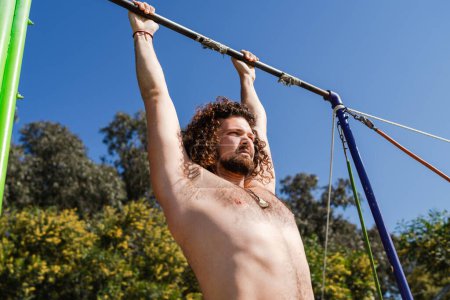 Photo for Curly and bearded man doing pull-ups on horizontal bar during his street workout - Royalty Free Image