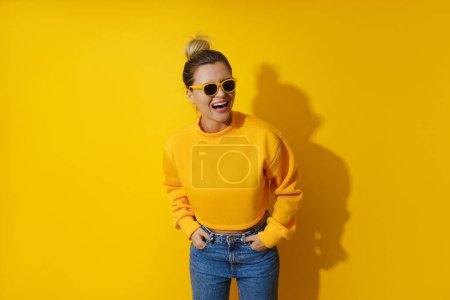Foto de Retrato de niña alegre con sudadera amarilla y gafas de sol sobre fondo amarillo - Imagen libre de derechos