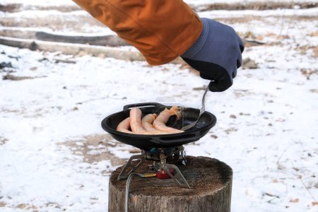 Téléchargez les photos : Saucisses au bowler dans la forêt en hiver. Faire de la nourriture camping. Aliments pour voyageurs dans les activités de plein air. - en image libre de droit