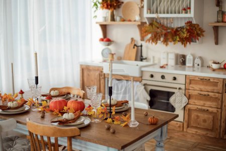 Téléchargez les photos : Intérieur de cuisine d'automne. Feuilles rouges et jaunes et citrouilles sur un fond clair. Servir la table du dîner - en image libre de droit