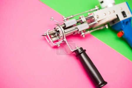 A tufting gun against a bright pinkang green colored background.