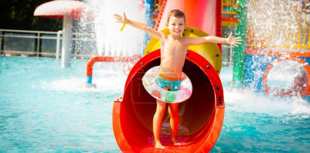 Téléchargez les photos : Joyeux garçon promenades sur le tube rouge toboggan du parc aquatique - en image libre de droit