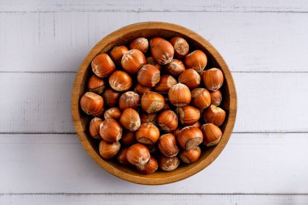 Photo for In shell hazelnuts bowl. Up view studio shoot isolated on light wooden background. - Royalty Free Image