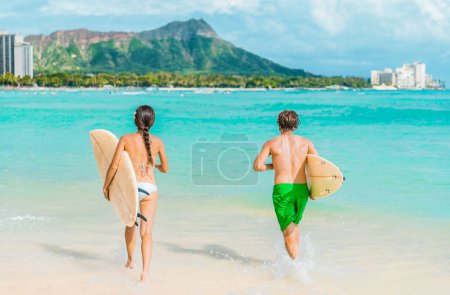 Hawaii Honolulu Paar Surfer beim Surfen auf Waikiki Strand mit Surfbrettern im Wasser laufen. Gesunde aktive Sport-Lifestyle-Fitness-Menschen in Diamantkopf-Berglandschaft.