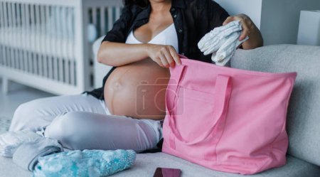 Pregnancy hospital bag. Pregnant woman preparing hospital bag for birth for mom and baby. Expectant mother packing diapers, baby clothing etc.