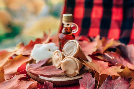 El jarabe de arce taffy conos postre con la botella tradicional y la mesa de tela a cuadros hojas rojas en la mesa. Comida local de Quebec.