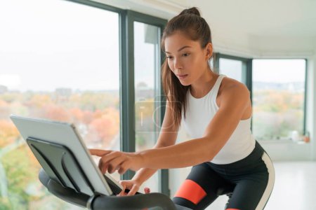 Home Fitness Workout Frauentraining auf intelligenten stationären Fahrrad drinnen vor dem Bildschirm online mit Live-Streaming-Abo-Service für Radsport-Übung verbunden. Junge asiatische Athletin.