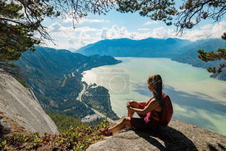 Hiking woman hiker in sitting looking at view of amazing nature landscape on famous Squamish Stawamus Chief Mountain Hike, British Columbia, Canada. Popular outdoor activity destination in Canada.