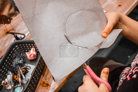 Las manos de los niños con tijeras cortando un círculo, artículos en miniatura en la mesa, niños haciendo bricolaje desde el ángulo superior