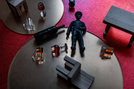 Crime scene with policeman, dropped chairs and alcohol glasses and bottle, red wine and beer spilled on the floor on red background and gold circles. Investigation image with miniature items search