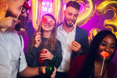 Happy multiracial friends having party in the club. Diverse people having fun while celebrating in the nightclub with funny party props. Nightlife and festive holidays concept. New Year's eve.