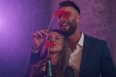Happy couple dancing on a party in a club while drinking and using funny face props