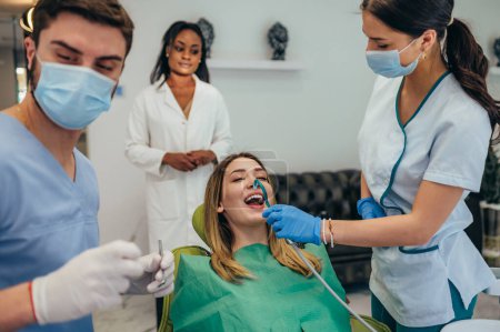 Junge Kaukasierin lässt sich beim Zahnarzttermin die Zähne checken. Patient auf Zahnarztstuhl repariert schmerzende Zähne. Gesundes Lächeln. Assistenten helfen Arzt bei einem Eingriff