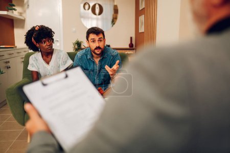 Diverse couple on a therapy session at marriage and family therapist's office having relationship problem. Young multiracial people trying to resolve conflict with help of professional psychologist.