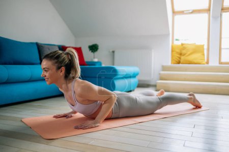 Jeune femme sportive pratiquant le yoga à la maison et faisant de l'exercice Double Leg Kicks tout en étant couché sur un tapis de fitness dans un salon. Mode de vie sain. pose de salabhasana.