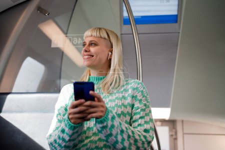 Portrait d'une femme qui se rend à l'école ou au travail en train ou en métro en utilisant un téléphone intelligent. Une jeune femme lit des courriels ou tape un message sur un téléphone portable pendant son trajet. Espace de copie.