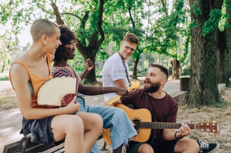 Group of multicultural environmentalists sitting in nature with guitar and singing songs on earth day. Interracial activists singing songs and celebrating earth day while promoting ecology. Subculture