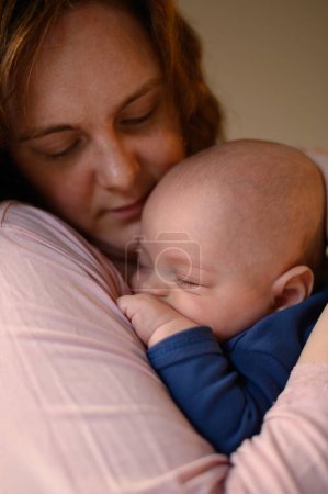 Mother playing and bonding with her sleepy baby boy at home while holding him in her arms