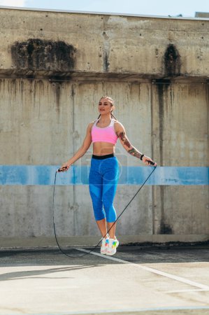 Attractive young woman using a fitness jump rope while training outside in an urban environment