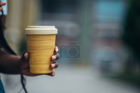 Main d'une femme afro-américaine tenant une tasse de café réutilisable faite d'un matériau écologique