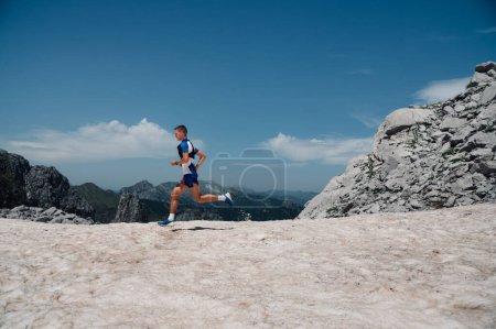 An extreme sportsman is running an ultramarathon, skyrunning and trail running on mountain range on sunny day in wild nature. A skyrunner is running fast a marathon in mountain range. Copy space.