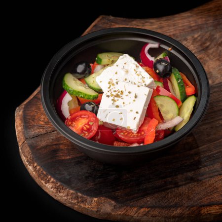 Téléchargez les photos : Salade grecque fraîche avec poivre, tomate, olive, fromage feta. Aller Salade dans un arc noir, plat sur un plateau, espace de copie, nourriture pour le menu et la publicité. gros plan - en image libre de droit