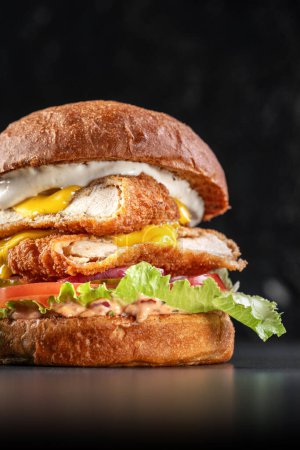 Photo for Smoked chickenburger centred on black backgrounds with double schnitzel, onion, cheddar, iceberg lettuce, tomato and barbeque sauce. Delicious burger beef and bacon , sandwich, fast food, delicious food - Royalty Free Image