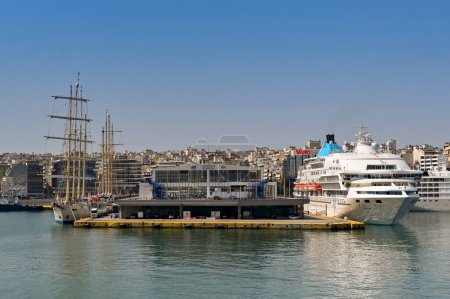 Foto de Pireo, Atenas, Grecia - Junio 2022: Crucero Celestyal y veleros de mástil alto amarrados en una de las terminales de cruceros en el puerto del Pireo. - Imagen libre de derechos