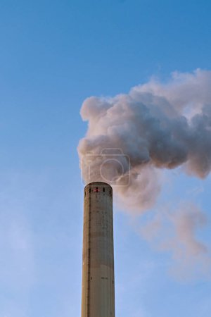 Photo for Smoke belching out of a tall chimney stack at a power station. No people. Copy space. - Royalty Free Image