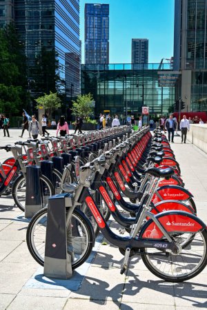 Foto de London, England, UK - June 2022: Bicycles for rent parked in front of office buildings in Canary Wharf. The bikes are sponsored by Santander bank. - Imagen libre de derechos