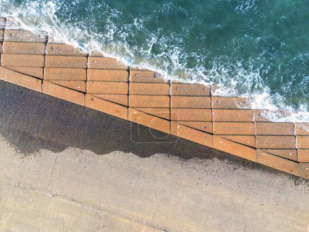 Photo for Aerial view of waves breaking over the concrete steps of a promenade at high tide. - Royalty Free Image