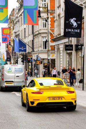 Photo for London, England, UK - 27 June 2023: Rear view of a yellow Porsche Carrera 911 Turbo S driving along New Bond Street in central London,. - Royalty Free Image