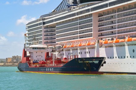 Foto de La Valeta, Malta - 6 de agosto de 2023: Gran crucero MSC Divina atracado en el puerto de la ciudad con un pequeño petrolero alonsgide para repostar - Imagen libre de derechos