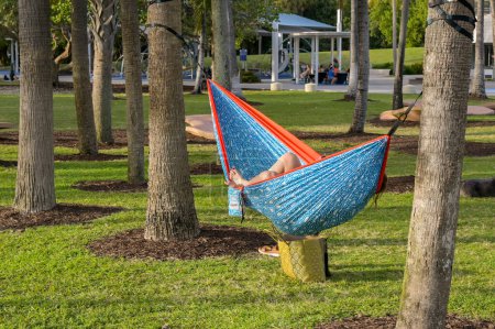 Photo for Miami, Florida, USA - 1 December 2023: Person lying in a hammock between palm trees in the public park near South Pointe at the end of Miami's South Beach - Royalty Free Image
